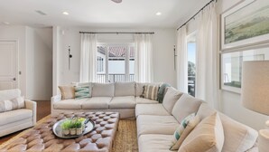 Una sala de estar con un sofá modular, un reposapiés de cuero marrón y un ventanal con cortinas.
