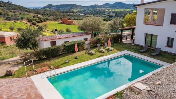 Ein Schwimmbad mit Blick auf die Landschaft, ein kleiner Garten und ein weißes Gebäude mit Balkon.