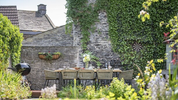 Un bâtiment en pierre recouvert de lierre, un jeu de fléchettes et une table avec des chaises, le tout situé dans un jardin.