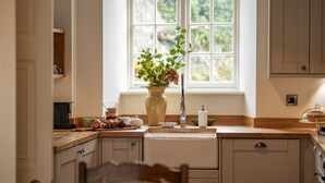 Une cuisine avec une fenêtre, des placards en bois, un évier et un vase rempli de fleurs.
