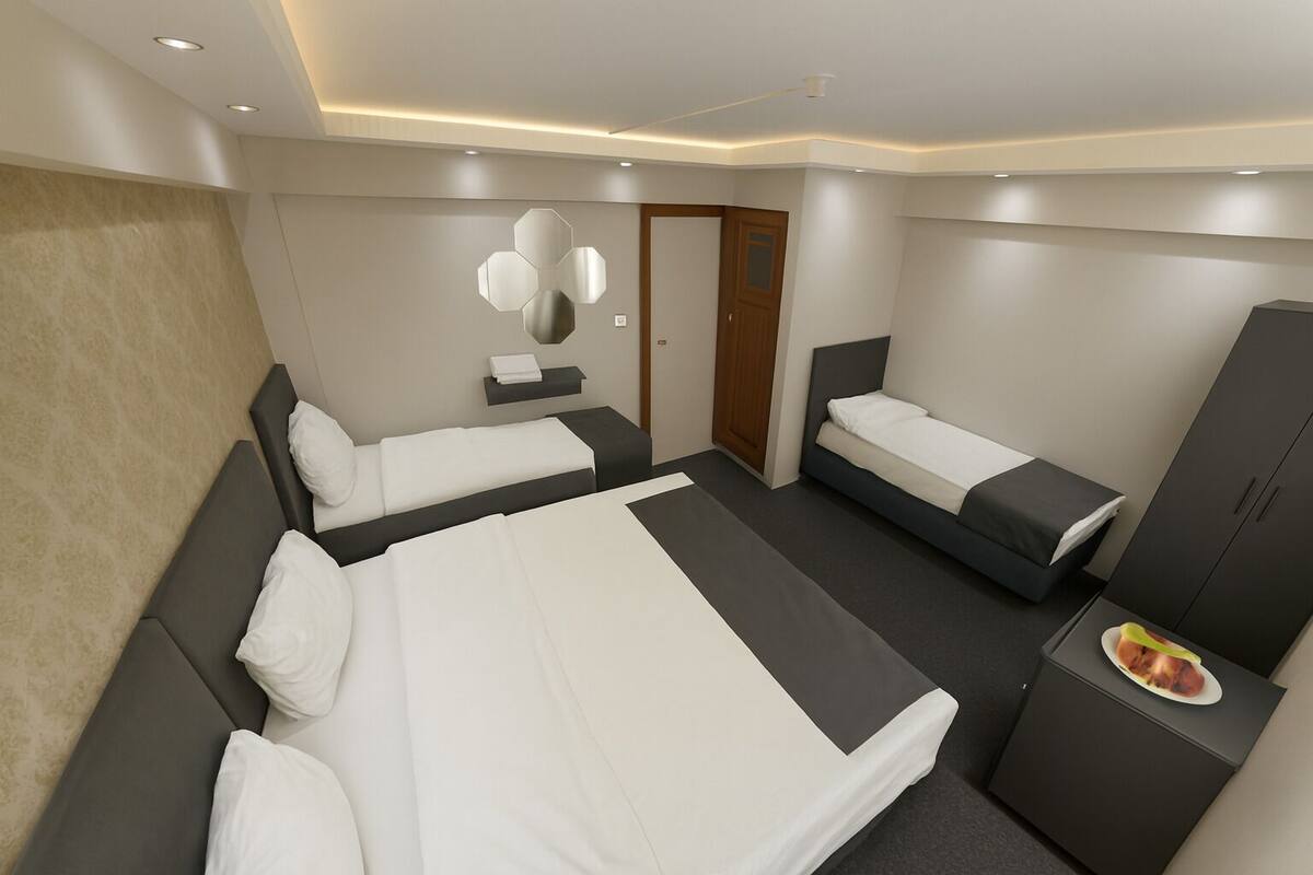 Una habitación de hotel moderna con una cama grande, dos camas más pequeñas, un armario y un espejo en la pared.