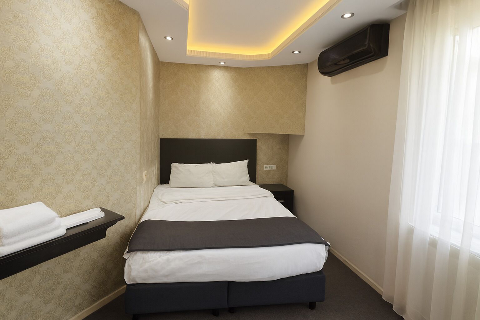 Een hotelkamer met een bed, nachtkastjes, een aan de muur bevestigde televisie en een raam met gordijnen.