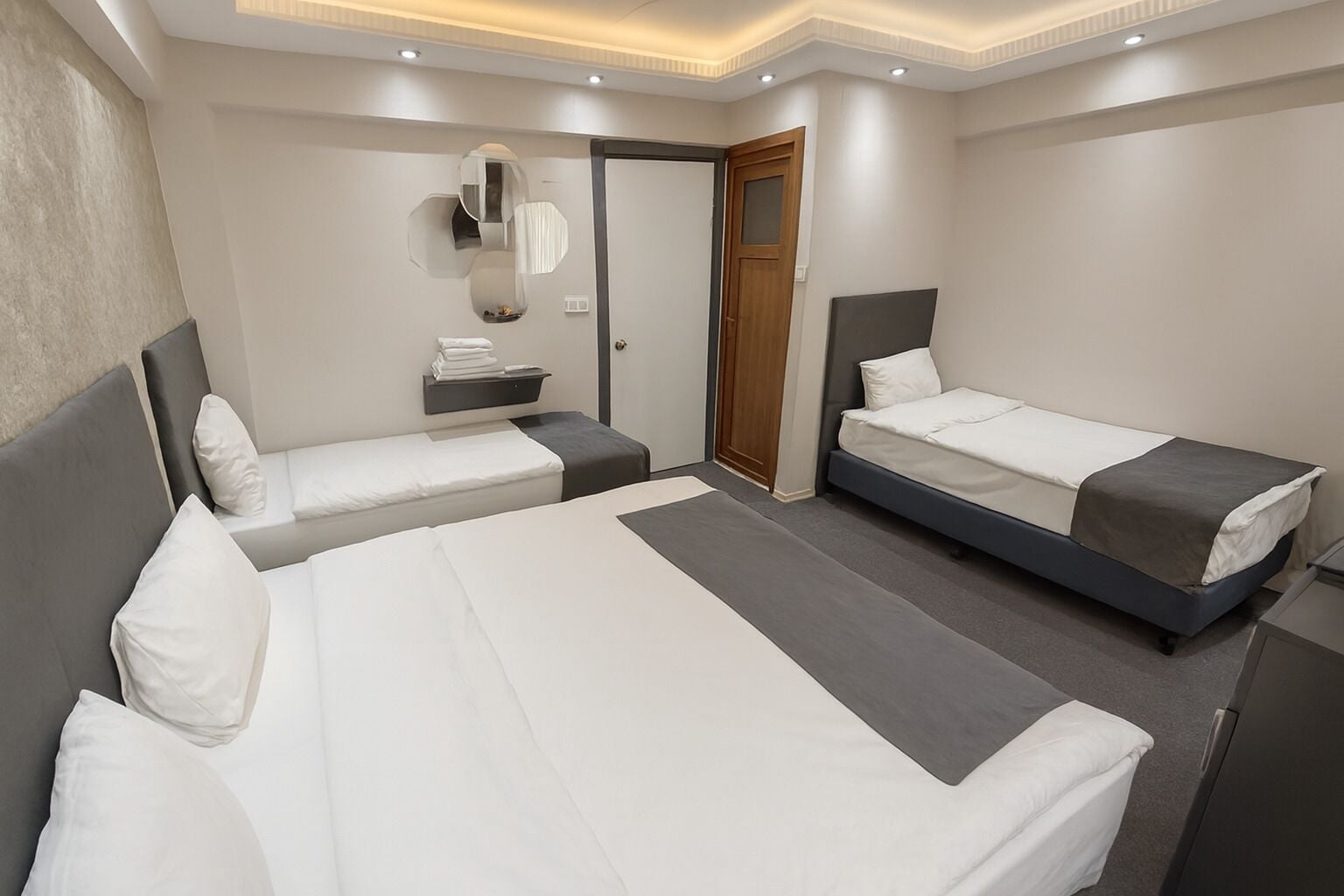 A modern hotel room with two single beds, a small seating area, a mirror, and a door.