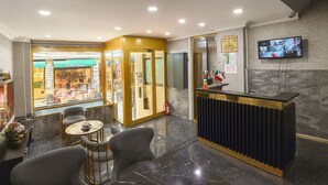Un hall de hotel con recepción, zona de estar y vistas a la calle.