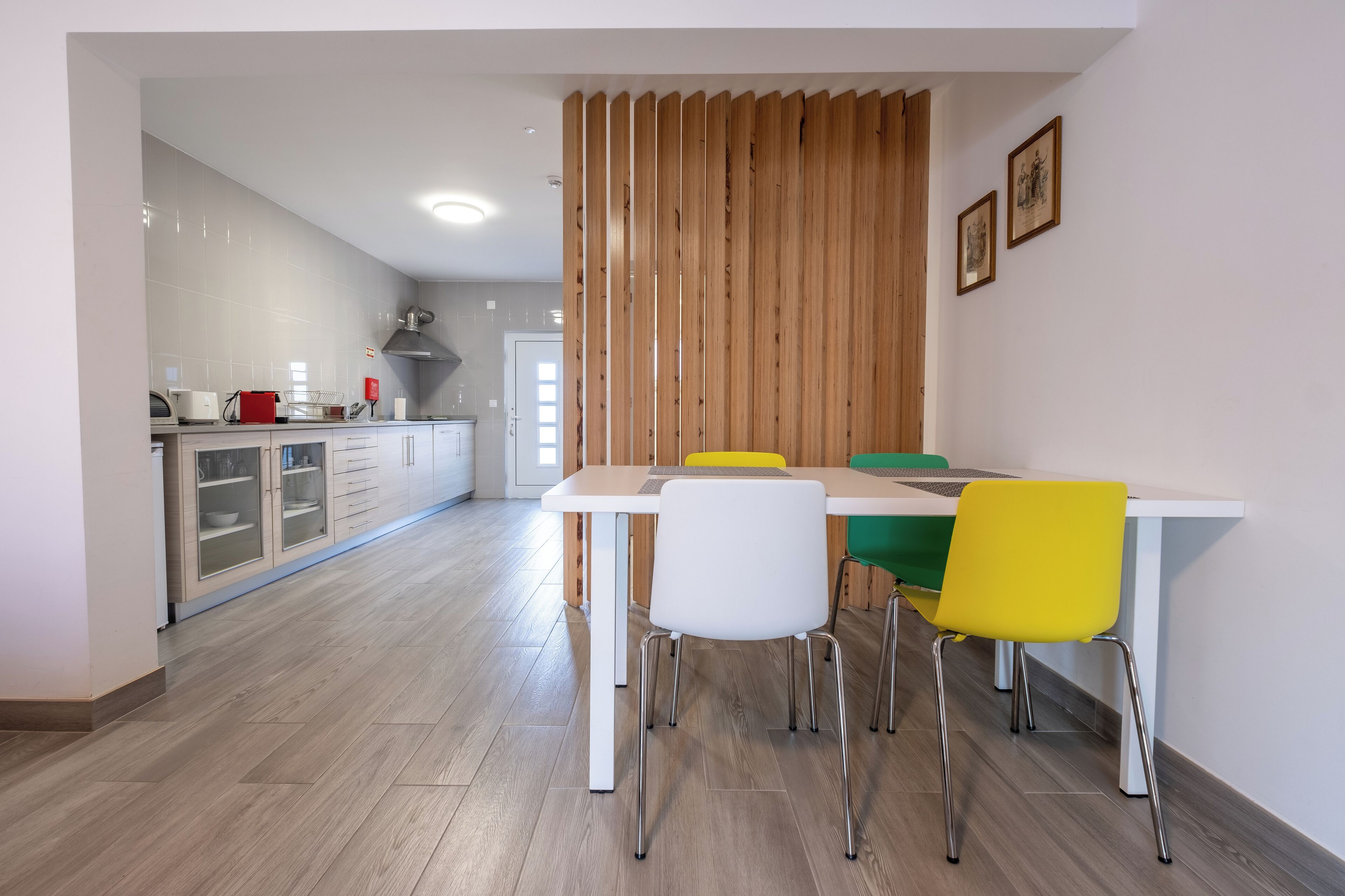 A modern kitchen with white cabinets, a wooden partition, and a dining area with a white table and yellow chairs.