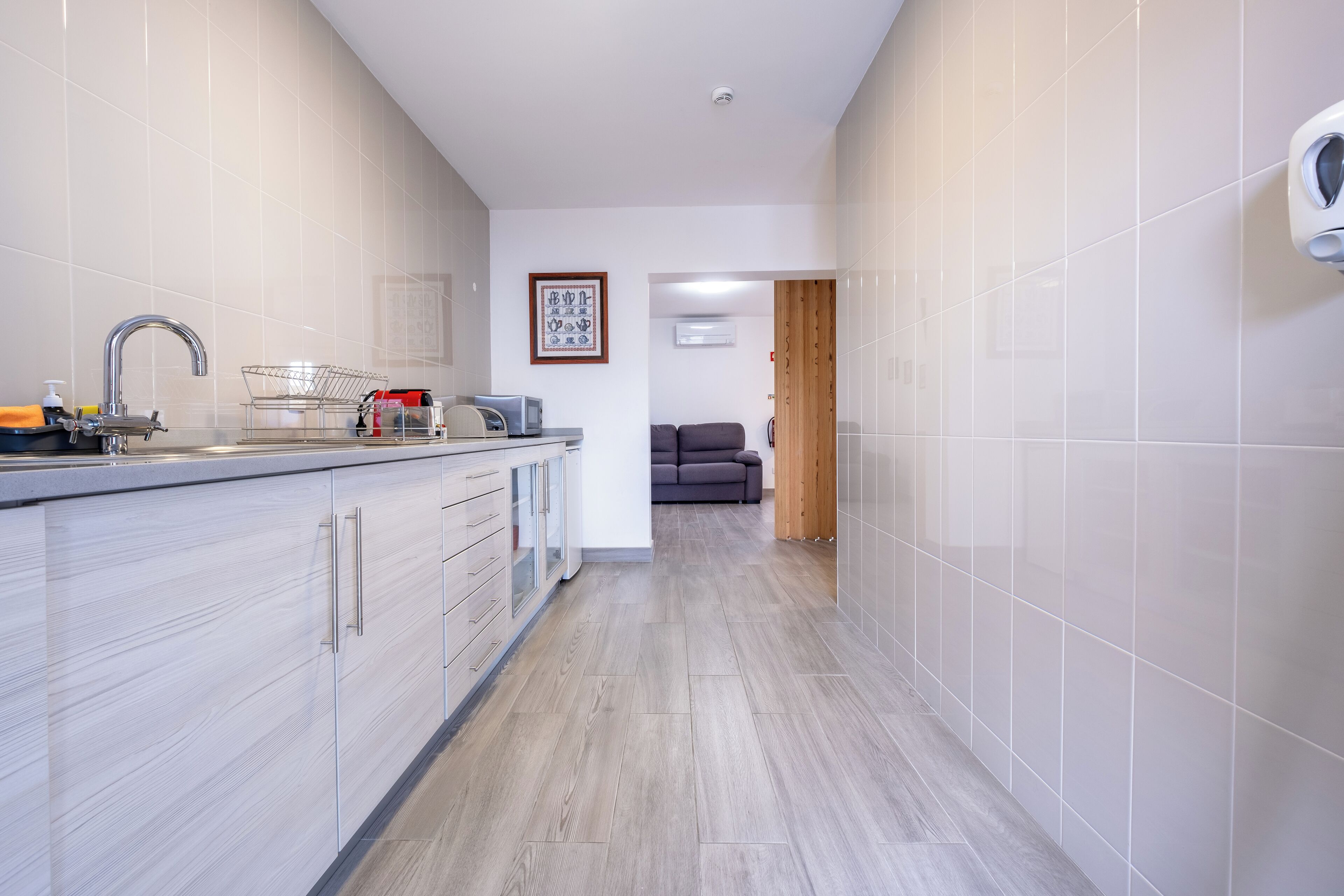 Eine moderne Küche mit integriertem Geschirrspüler, Spüle mit Armatur und Mikrowelle. An der Wand hängt ein gerahmtes Bild und eine Holztür führt in einen anderen Raum.