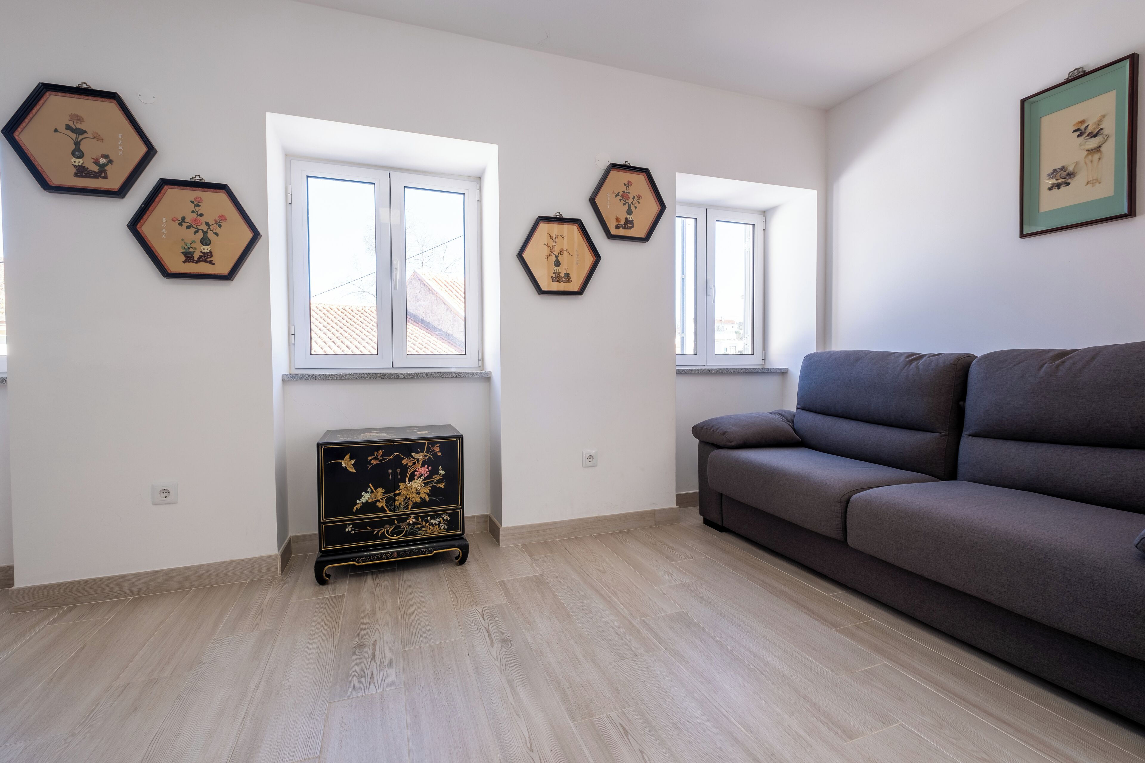 Una sala de estar con un sofá gris, suelo de madera y decoración mural hexagonal.