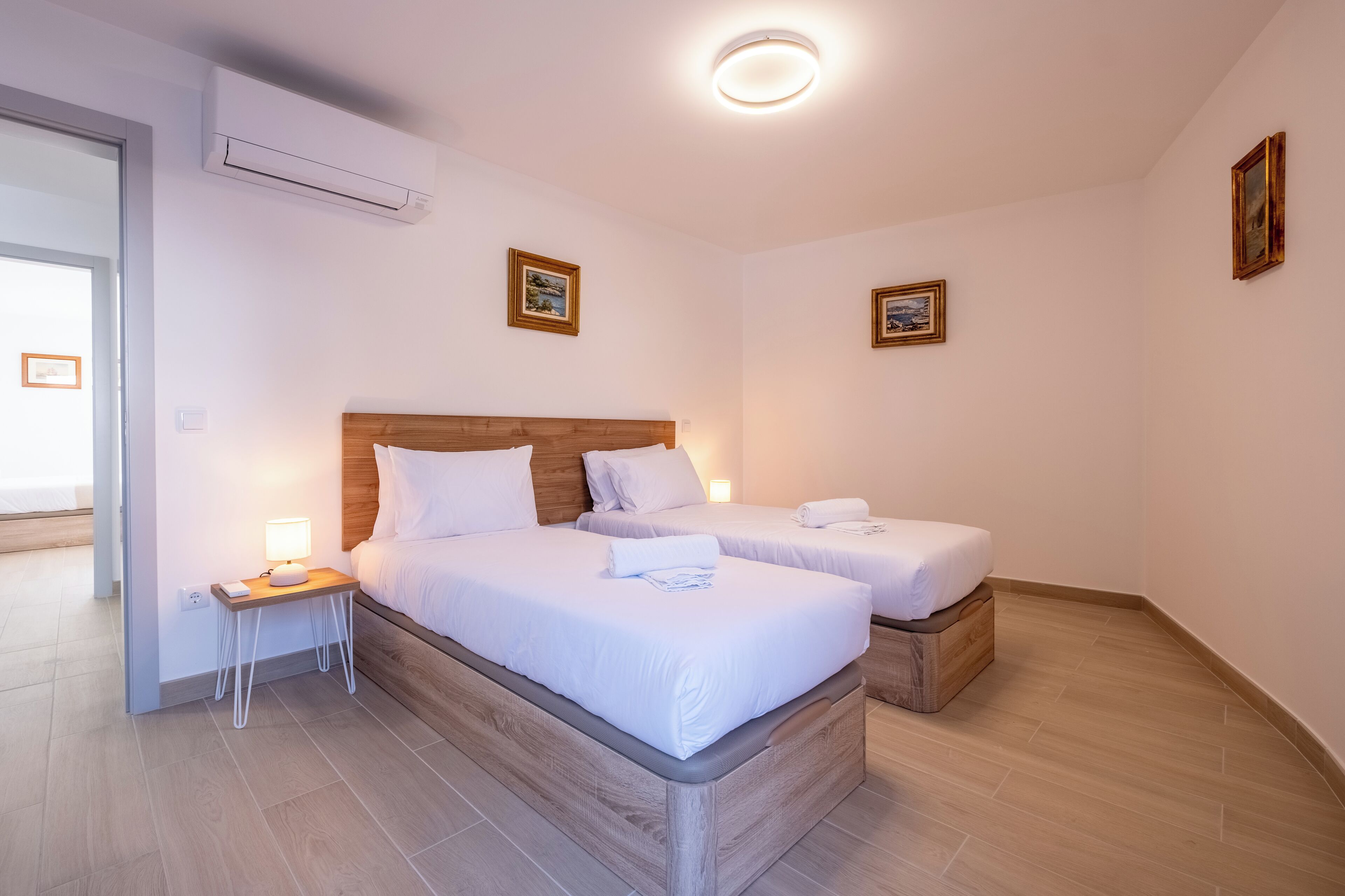 Een hotelkamer met twee bedden, een nachtkastje met een lamp en ingelijste foto’s aan de muur.