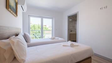Un dormitorio con dos camas, un ventanal grande, una puerta y un cuadro en la pared.