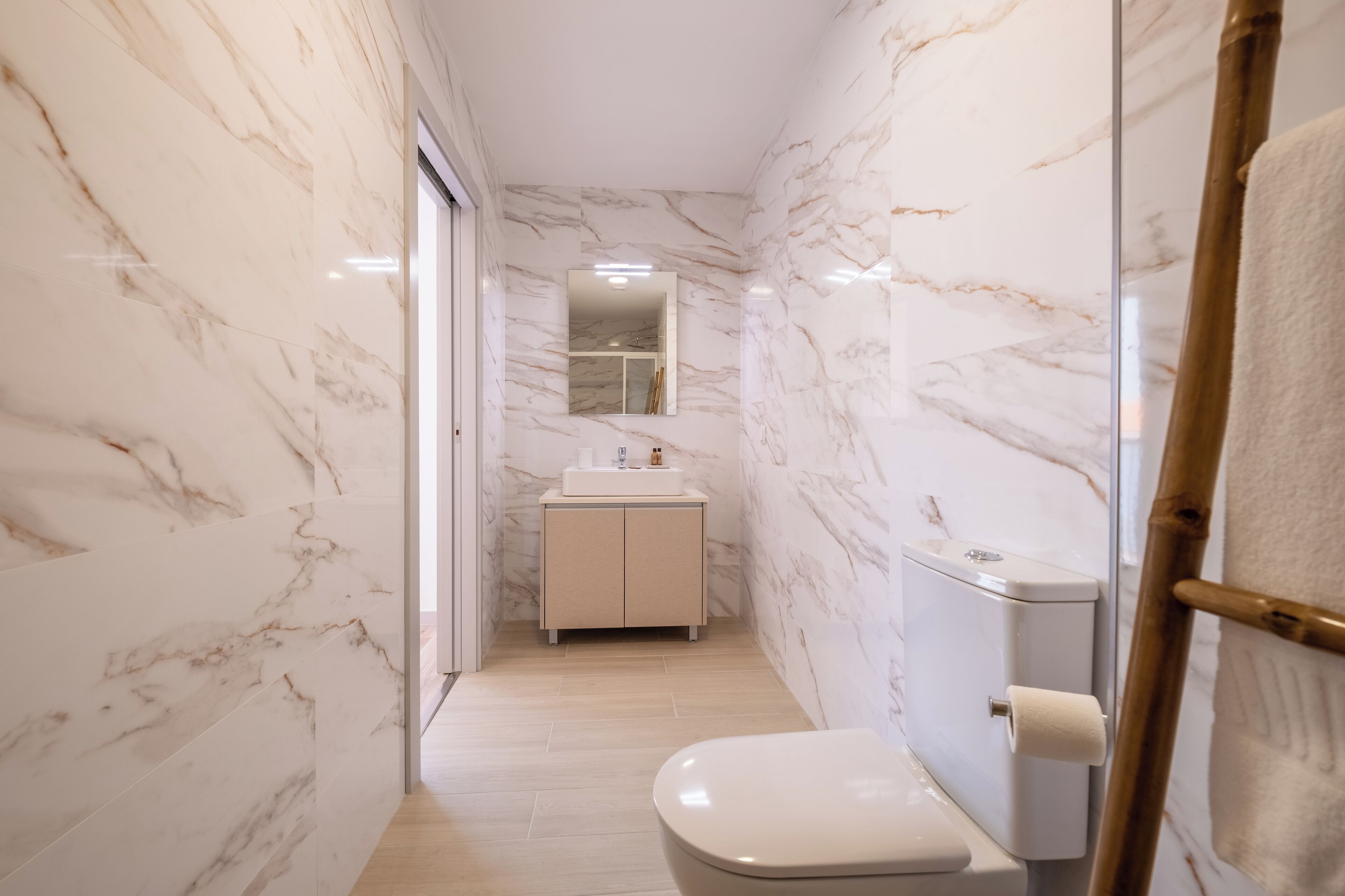 Un baño estrecho con paredes de mármol, un inodoro, un lavabo y un espejo.