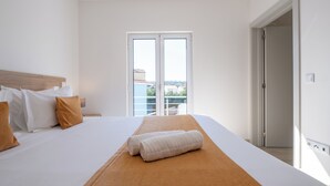 A hotel room with a bed, a view through a sliding glass door, and a door leading to another room.