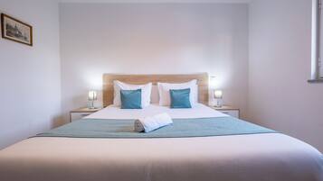 A neatly made bed with a wooden headboard, two bedside lamps, and a rolled towel on the bed.