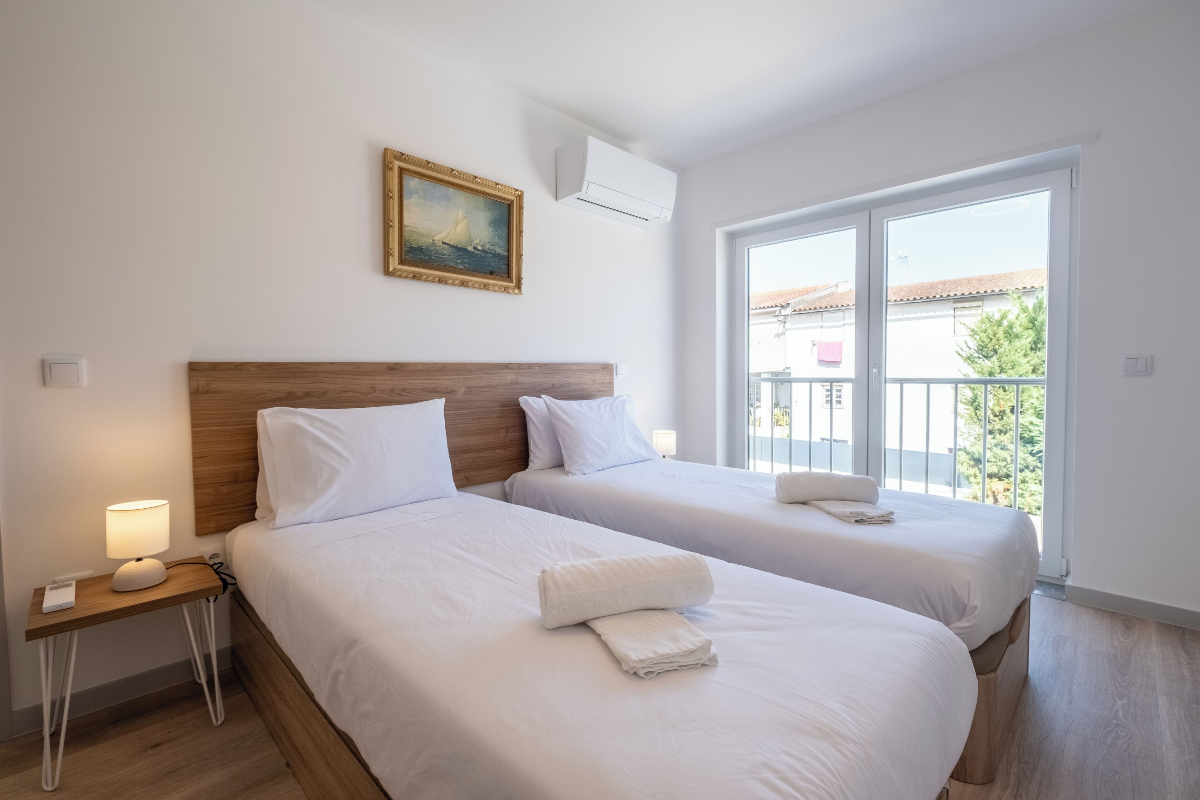 Een hotelkamer met twee bedden, een houten hoofdeinde, een schilderij, een airconditioner en een balkon met uitzicht.