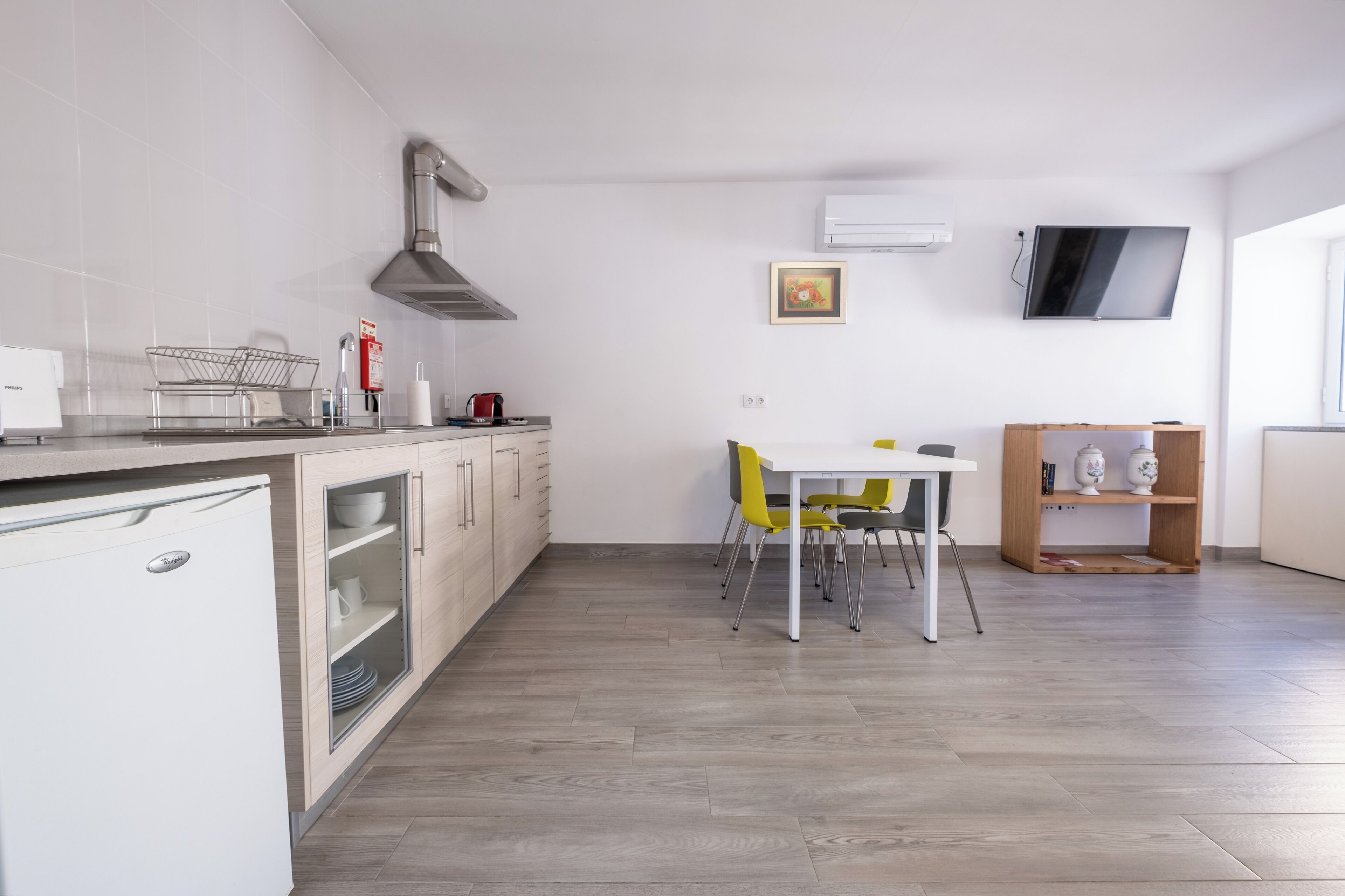 Una cocina moderna con armarios blancos, lavavajillas integrado y una zona de comedor con mesa blanca y sillas amarillas.