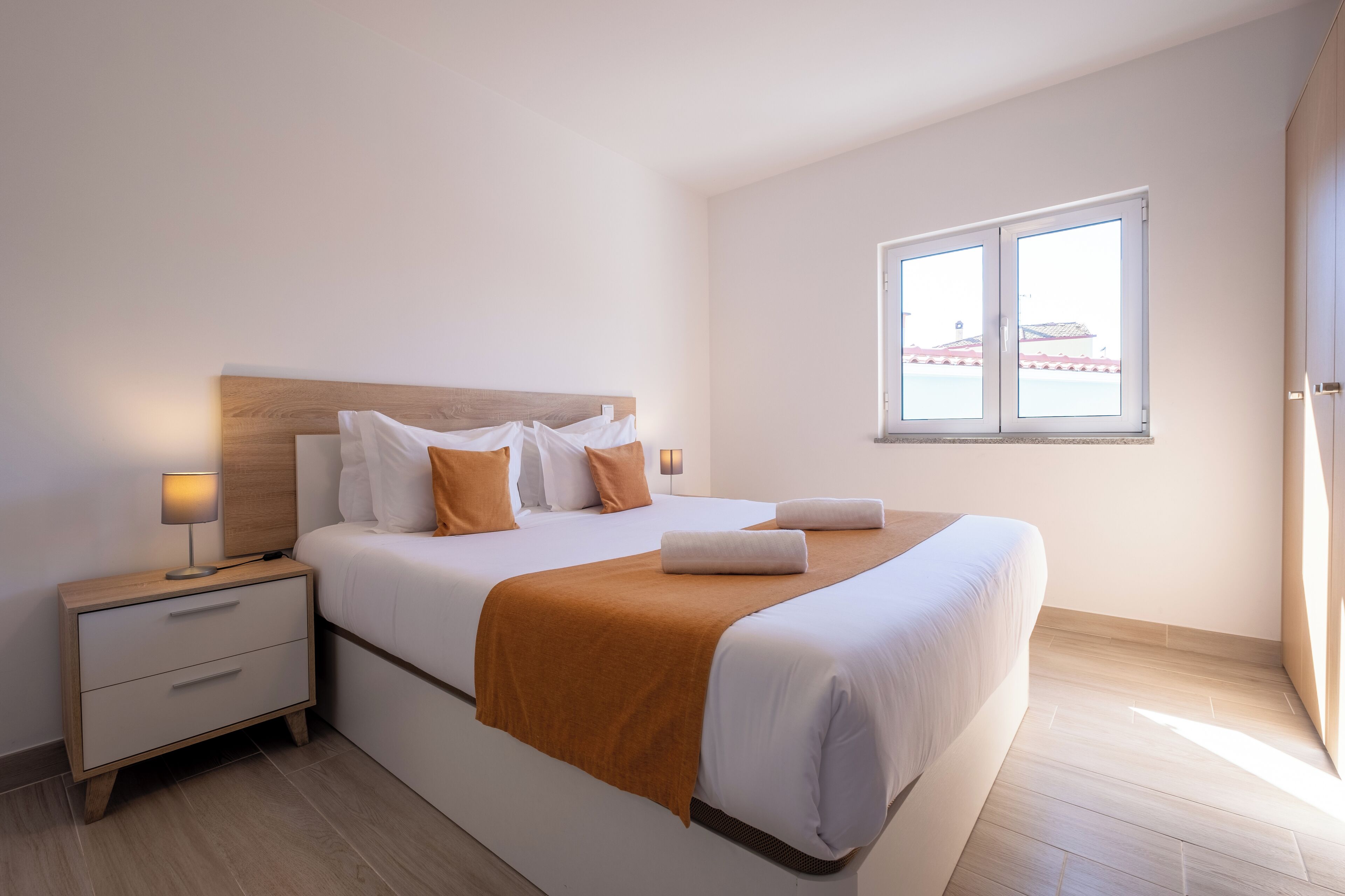 Una moderna camera d'hotel con un letto grande, un comodino, una lampada da letto e una finestra con vista su un edificio.