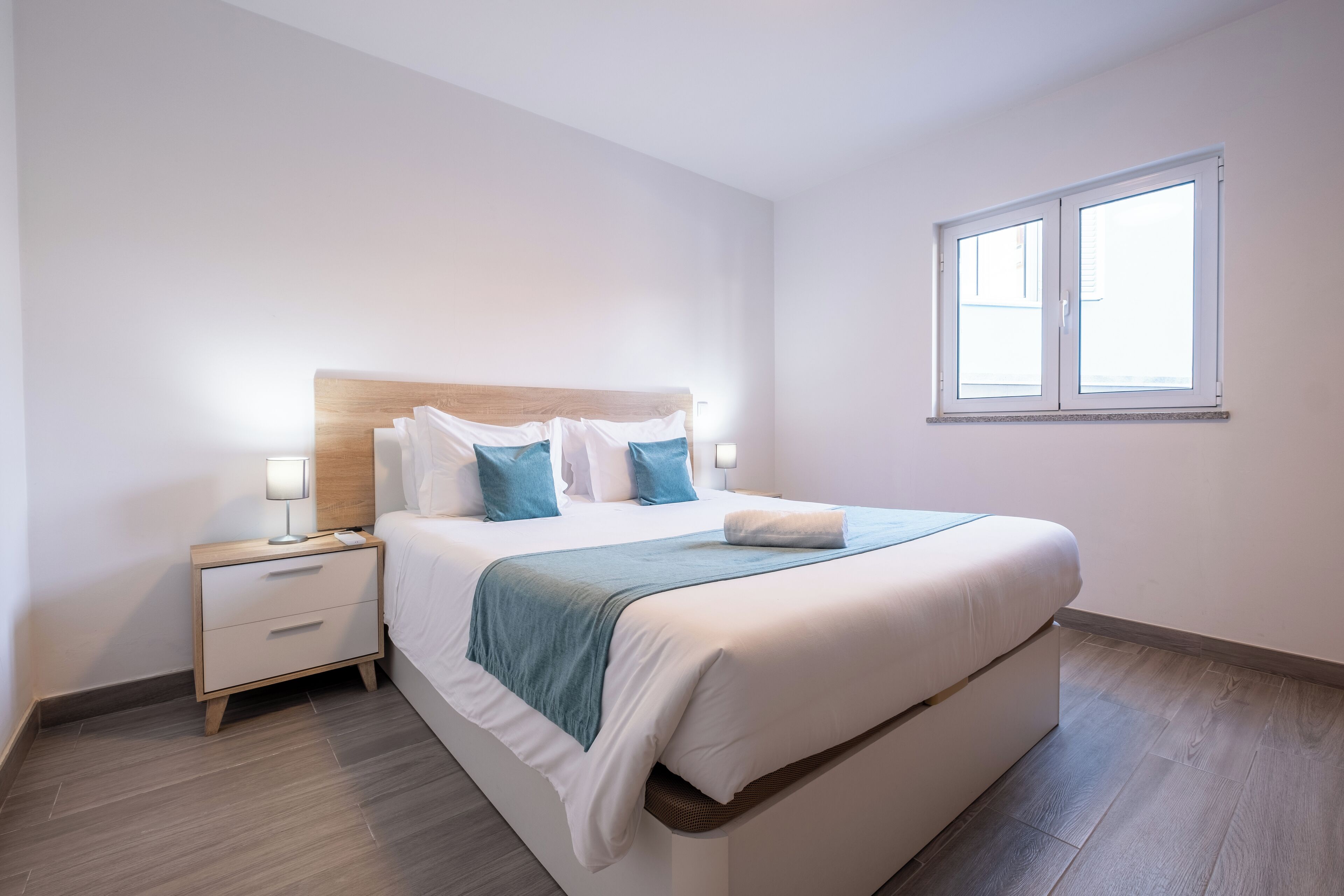 Habitación de hotel ordenada con cama, mesita de noche y ventana.