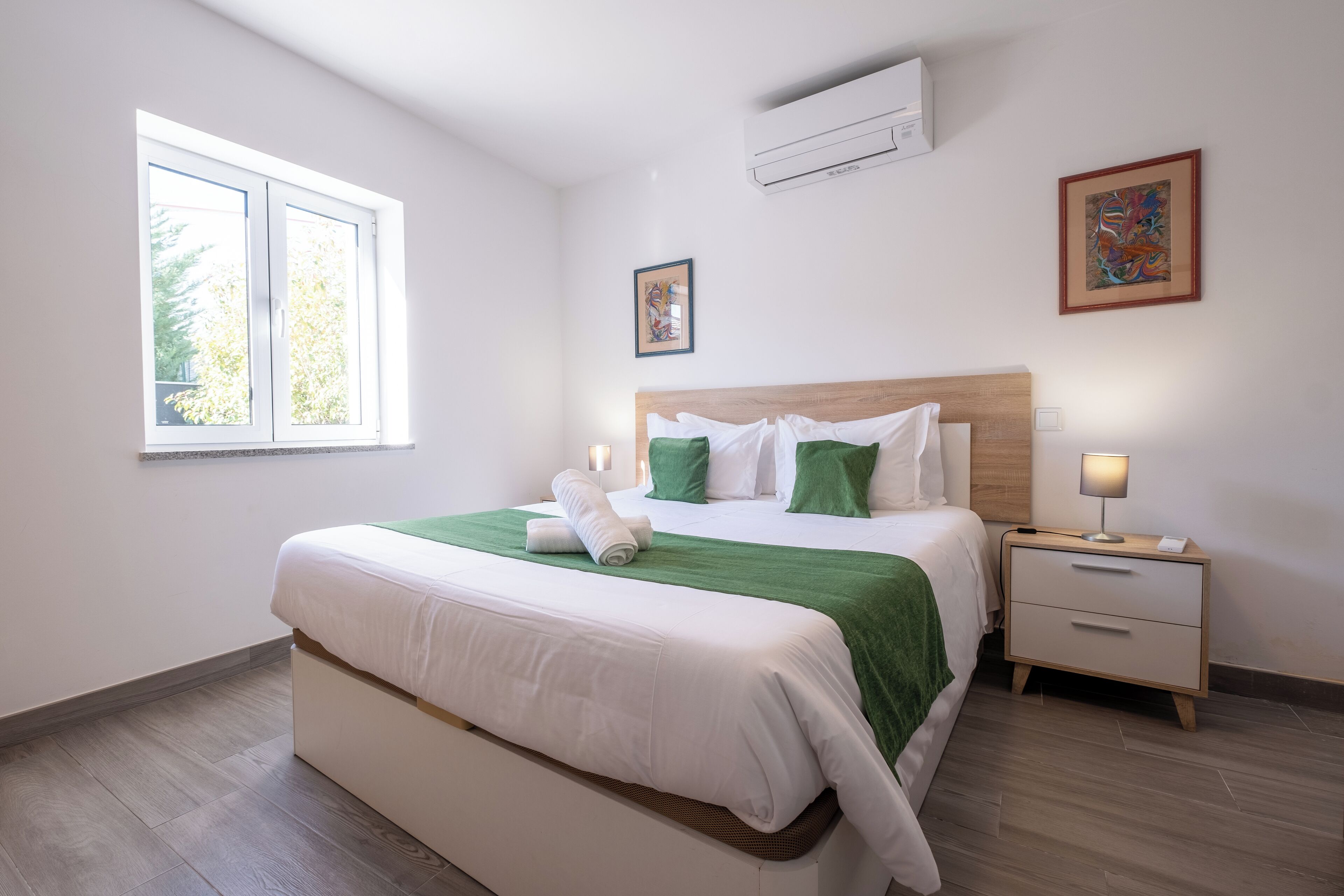 Un dormitorio ordenado con una cama grande, una mesita de noche y una ventana.