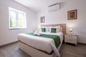 Un dormitorio ordenado con una cama grande, una mesita de noche y una ventana.