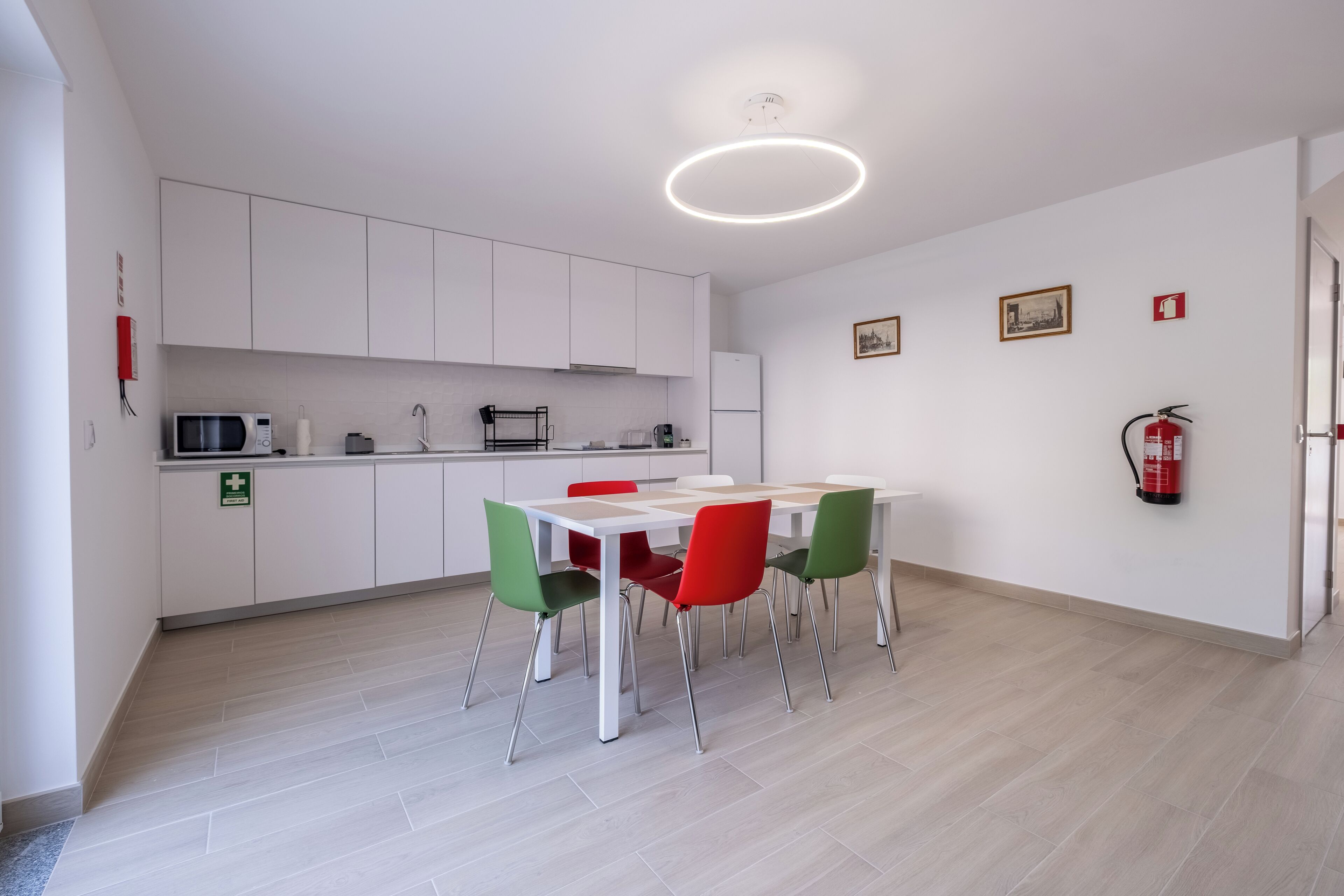 A modern kitchen with white cabinets, a dining table with red chairs, and a ceiling light fixture.