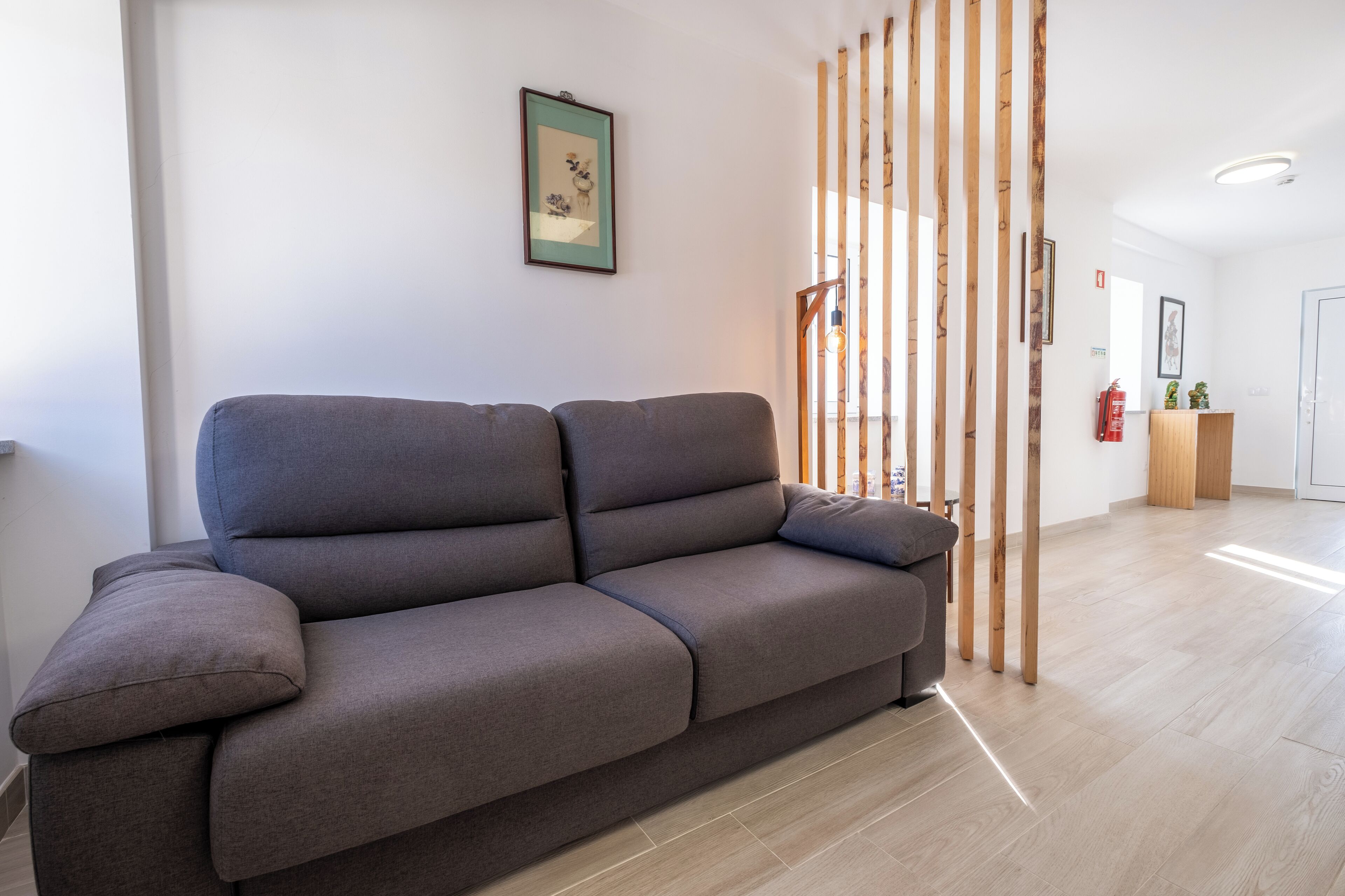 A modern living room with a grey sofa, wooden slats, and a framed picture on the wall.