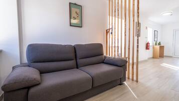 Ein modernes Wohnzimmer mit einem grauen Sofa, Holzlamellen und einem gerahmten Bild an der Wand.
