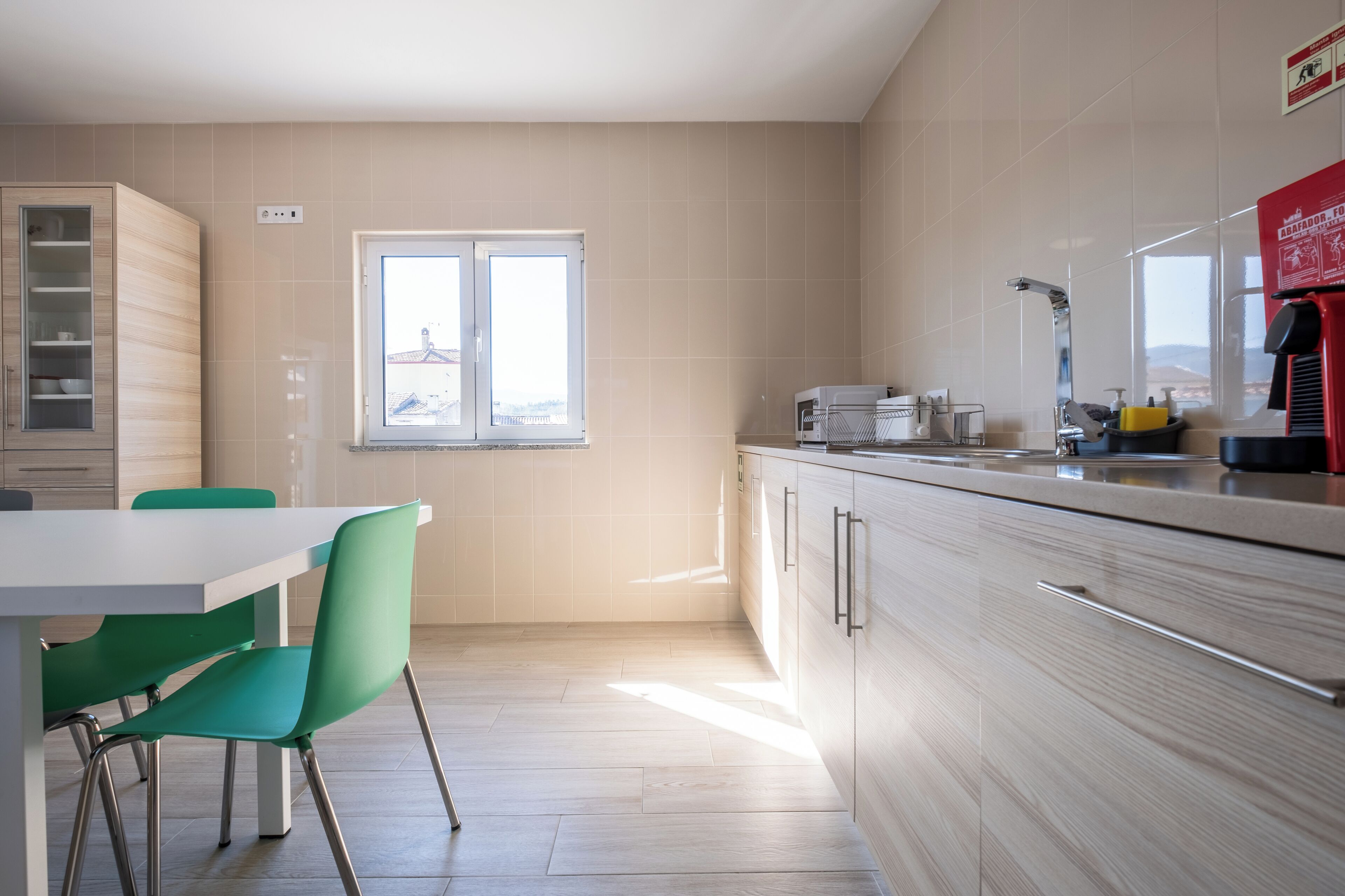 Una cocina moderna con comedor, que cuenta con un ventanal, armarios de colores claros y una encimera con electrodomésticos.