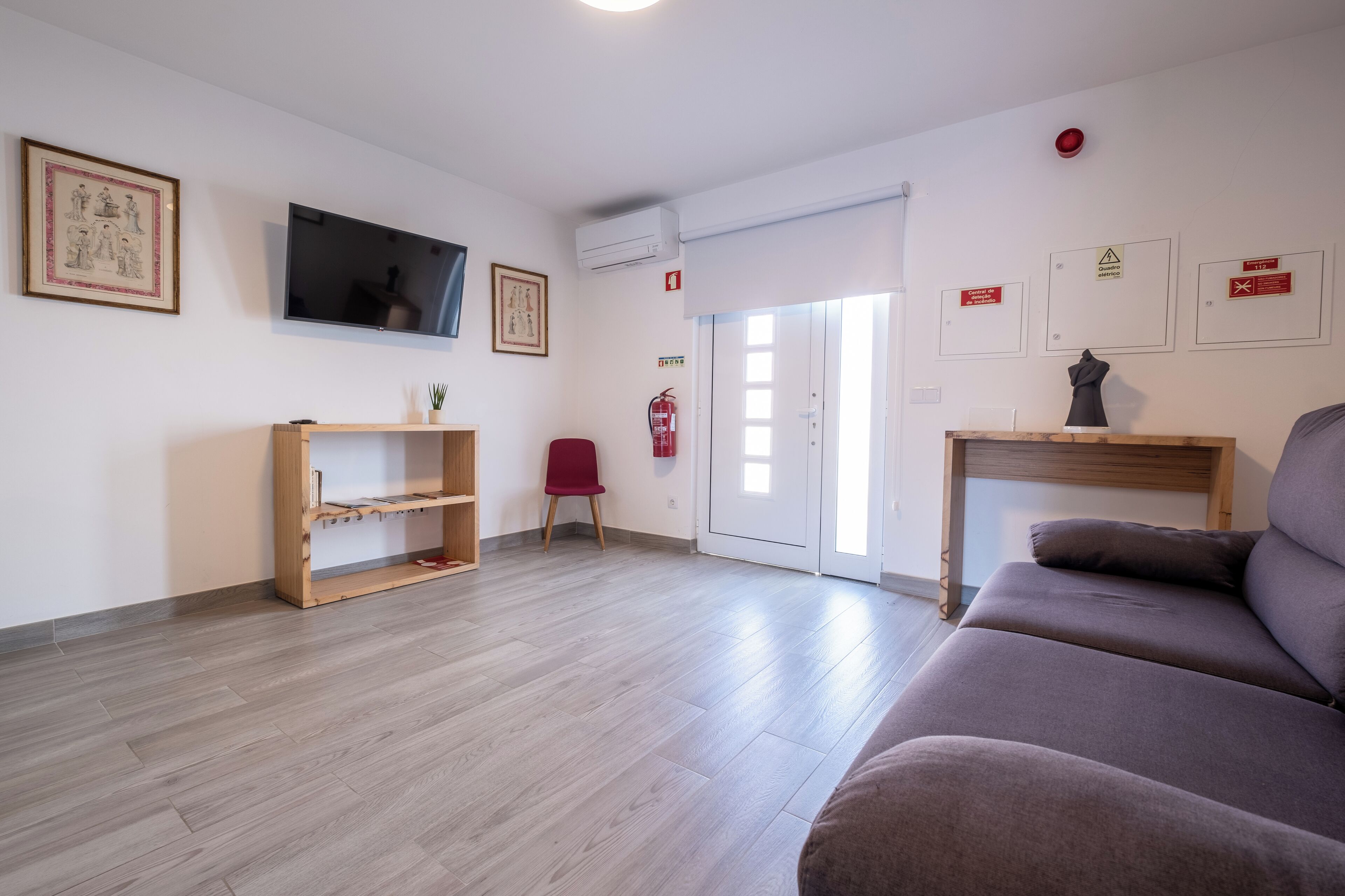 A living room with a sofa, a red chair, a wooden shelf, a flat-screen TV, and a fire extinguisher.