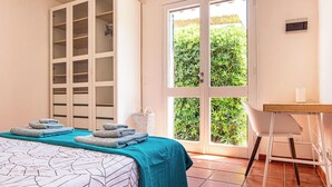 Ein Schlafzimmer mit Bett, Kleiderschrank, Schreibtisch und Blick auf Grün durch eine Glastür.