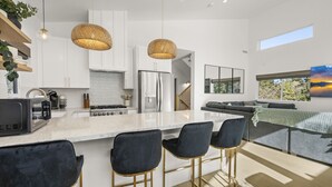 Una cocina moderna con armarios blancos, una isla grande con taburetes de bar y un comedor con vistas al exterior.
