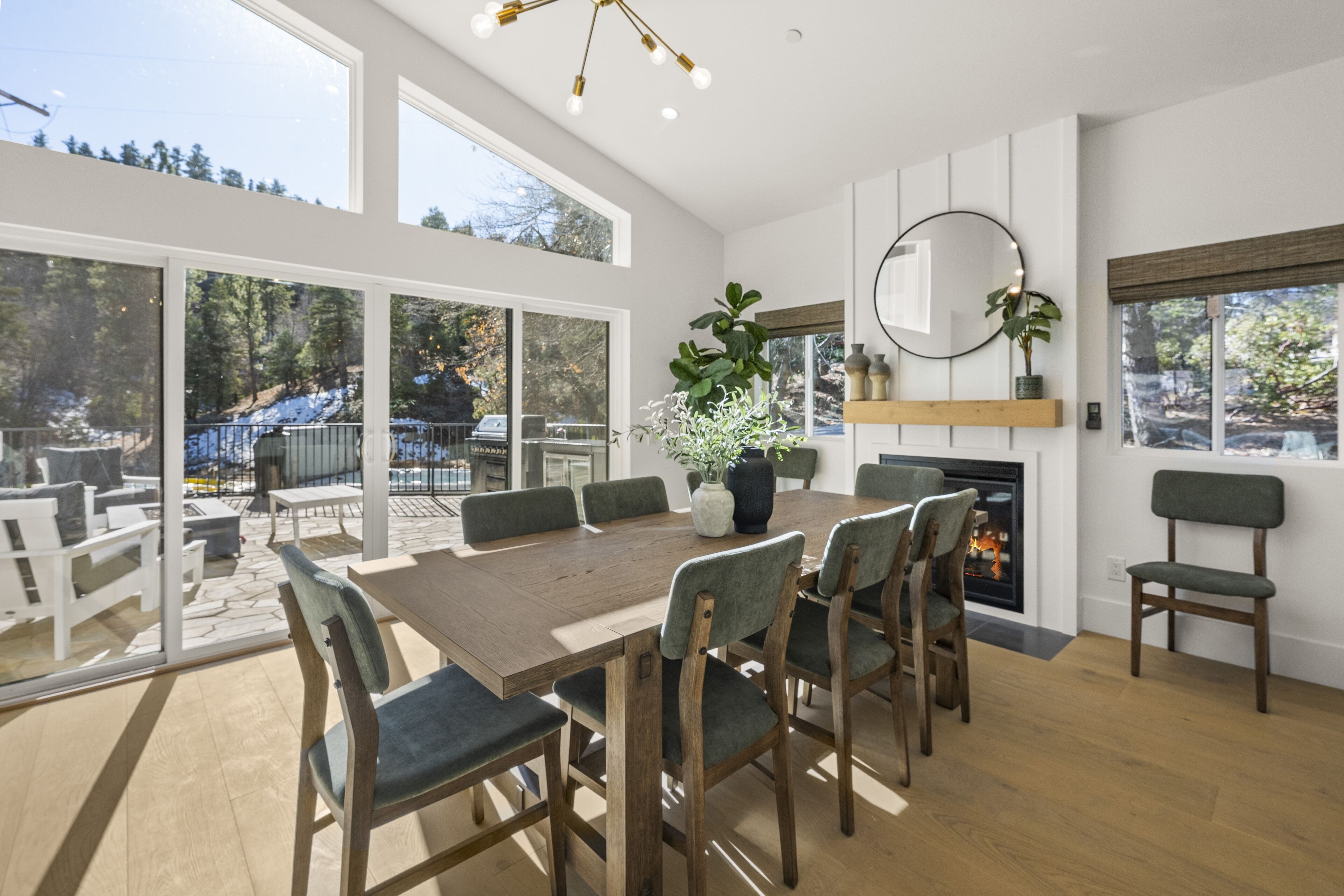 A spacious dining area with a large wooden table and chairs, a fireplace, and large windows offering a view of the outdoors.