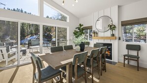 Un comedor amplio con una gran mesa de madera y sillas, una chimenea y ventanas grandes que ofrecen vistas al exterior.
