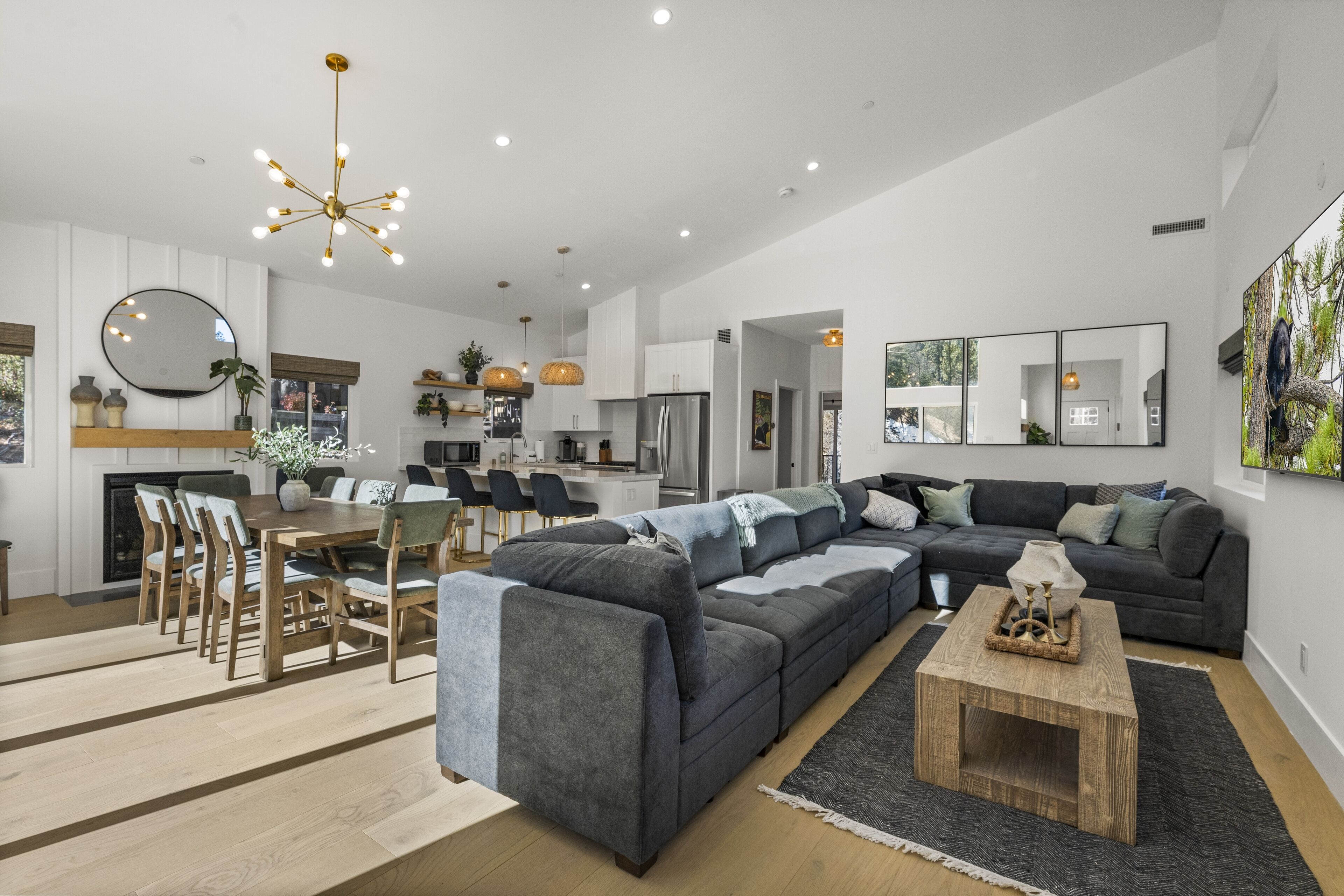 A modern living room with a sectional sofa, a dining area with a wooden table and chairs, and a kitchen in the background.