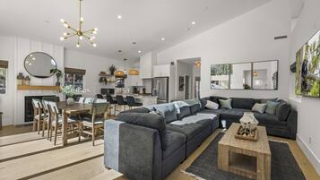 A modern living room with a sectional sofa, a dining area with a wooden table and chairs, and a kitchen in the background.
