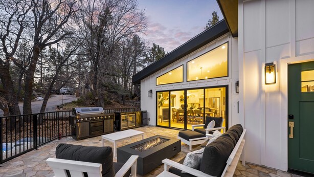 Un patio exterior moderno con suelo de piedra, mobiliario blanco y un hogar a leña integrado.