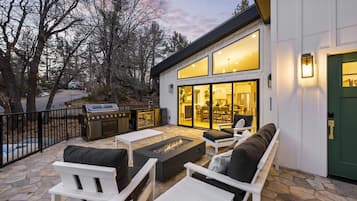 A modern outdoor patio with stone flooring, white furniture, and a built-in fire pit.