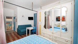 A bedroom with a bed, a wardrobe, a TV, a small table, and a blue sofa. - The Casello sul Mare is a historic railway house built in 1895 as a residence for railway workers and restored in 2025 while preserving its authentic charm. The property is set in a truly unique position, suspended between the railway and the sea, offeri (Torremuzza)