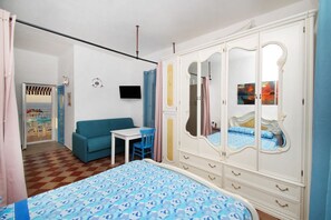 Una camera da letto con un letto, un armadio, una TV, un tavolino e un divano blu.