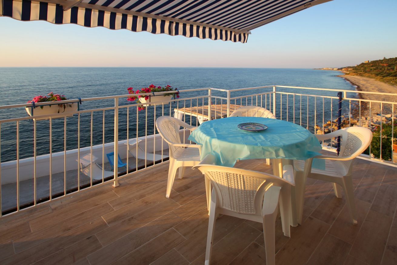 A balcony with a table and chairs overlooking the sea.