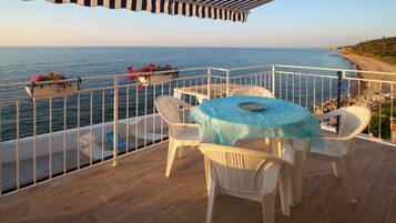 A balcony with a table and chairs overlooking the sea.