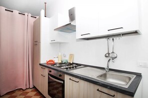 Una cucina compatta con piano cottura a gas, lavello e pensili bianchi.