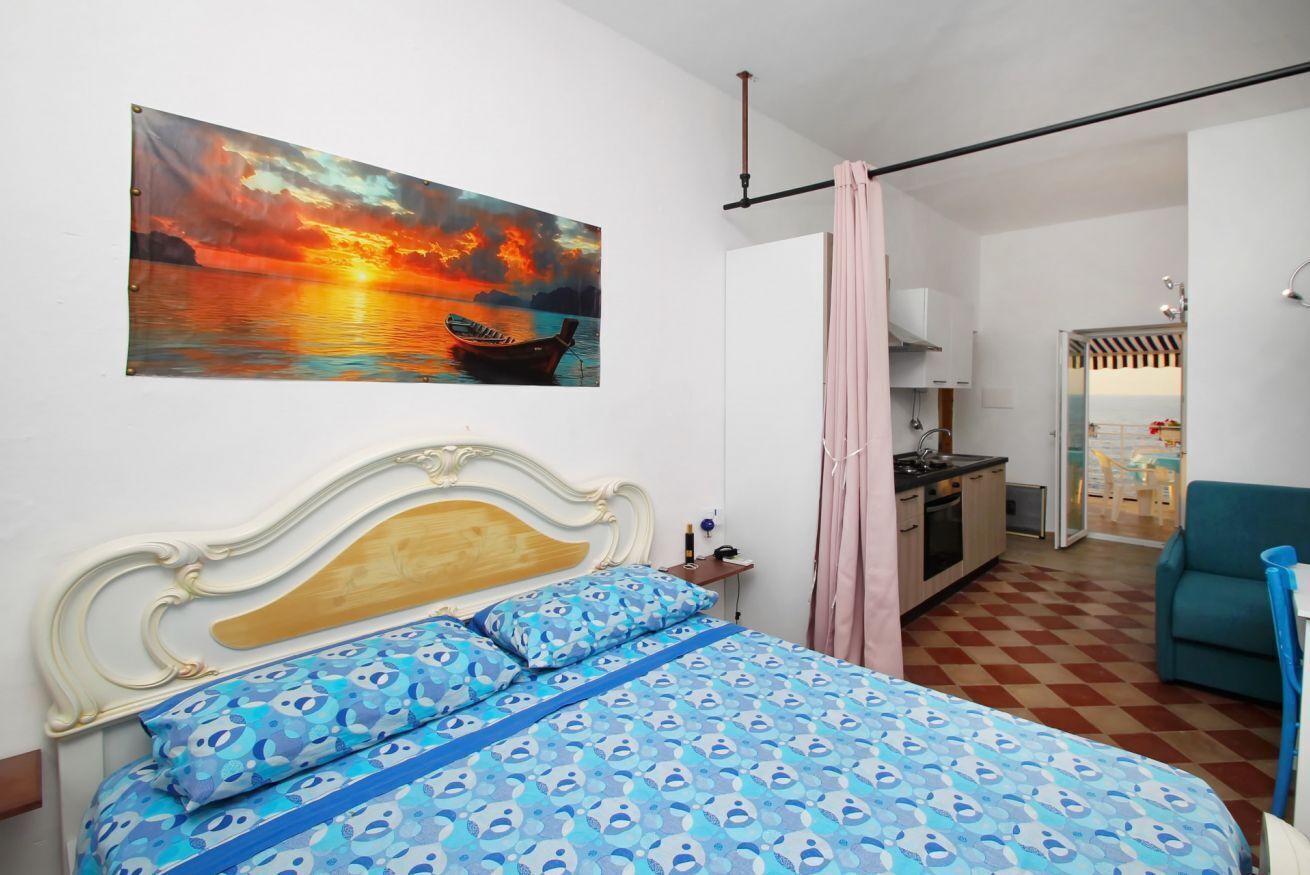 Un dormitorio con cama, un cuadro, una kitchenette y vista al mar.