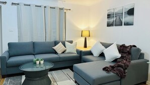 Una sala de estar moderna con un sofá gris, una mesa de centro redonda de vidrio y una mesita de noche con una lámpara.