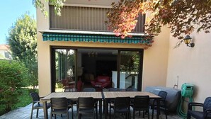 Ein Patio mit Steinfliesen, einem Esstisch mit Stühlen und einer überdachten Sitzecke.