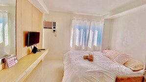 Ein Schlafzimmer mit Bett, Fernseher, Schreibtisch und einem Fenster mit Vorhängen.