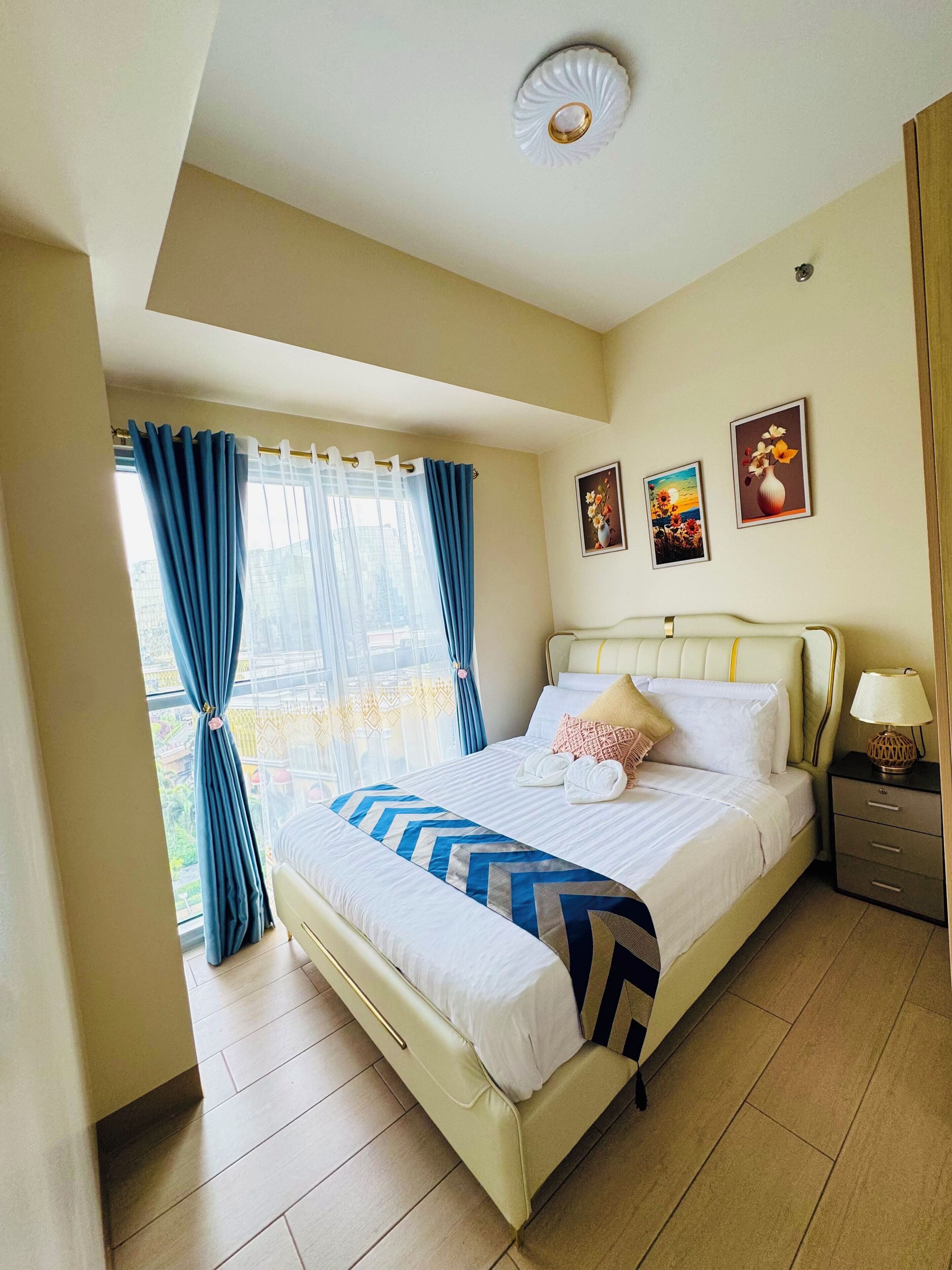 Une chambre d’hôtel avec un lit, une table de chevet, une fenêtre avec des rideaux et un luminaire au plafond.