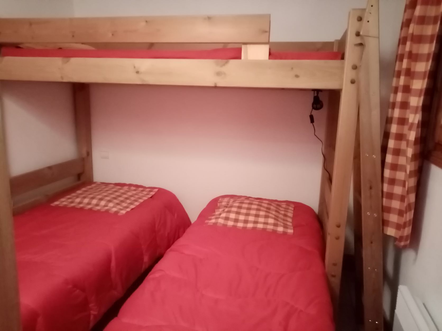 A bunk bed with two beds, each with a red bedspread and a checkered pillow.