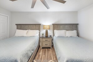Ein Doppelzimmer mit zwei Betten, einem Nachttisch mit Lampe und einem Deckenventilator.