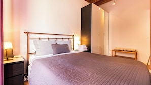 A neatly made bed with a headboard, a bedside table with a lamp, and a bench with towels. - Tapioles: Nice apartment with balcony in Poble Sec (Poble Sec)