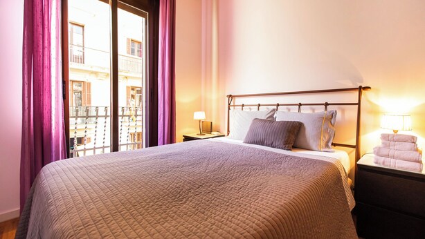A neatly made bed with a quilted blanket, a bedside lamp, and a nightstand with towels. - Tapioles: Nice apartment with balcony in Poble Sec (Poble Sec)