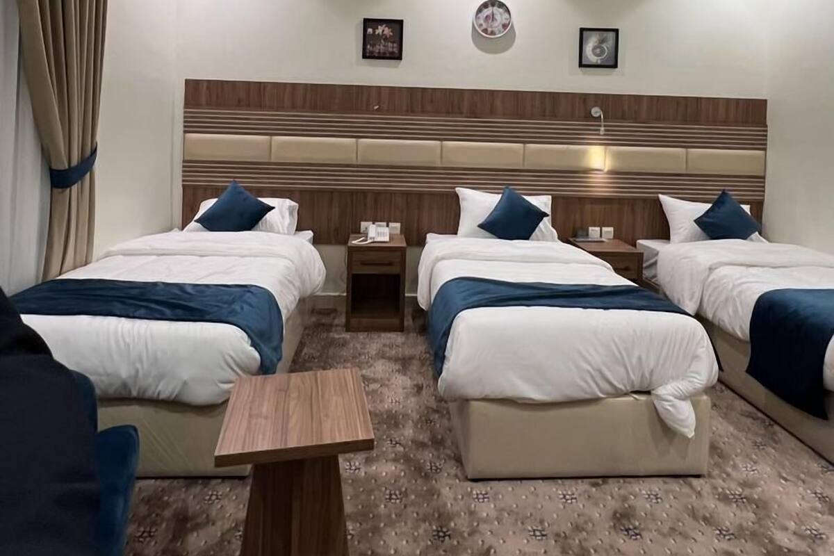 A hotel room with four beds arranged in a row, a wooden headboard, a small wooden table, and a patterned carpet.